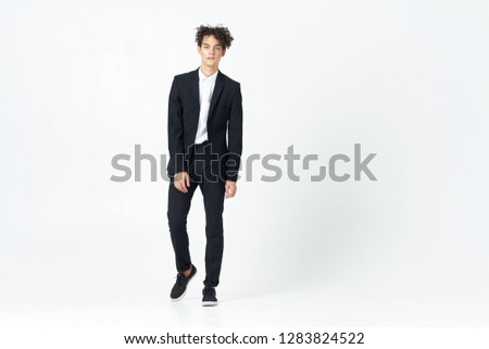 Cute man with curly hair in a suit in full growth on a light background
