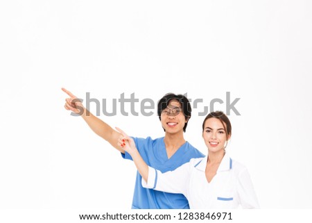Smiling doctors couple wearing uniform standing isolated over white background, pointing at copy space