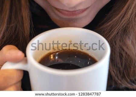 Closeup image of a beautiful Asian woman holding and drinking hot coffee with feeling good in cafe
