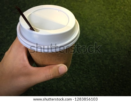 Hand grabing and holding cup of hot  coffee with green grass background. 