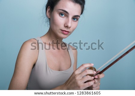 Close up portrait of a beautiful young woman posing with a violin isolated over blue background