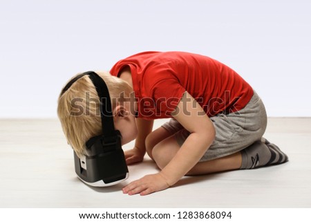 Little boy in a red shirt is experiencing virtual reality sitting on the floor. Isolate on white background. Technology concept.