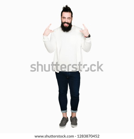 Young man with long hair and beard wearing sporty sweatshirt shouting with crazy expression doing rock symbol with hands up. Music star. Heavy concept.
