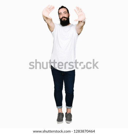 Young hipster man with long hair and beard wearing casual white t-shirt Smiling doing frame using hands palms and fingers, camera perspective
