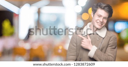 Young handsome man wearing winter coat over isolated background cheerful with a smile of face pointing with hand and finger up to the side with happy and natural expression on face