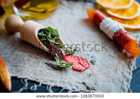 green tea mint leaves with strawberry in a wooden spoon, lemon slice, dry fruits roll and cup of tea on dark wooden background, copy space
