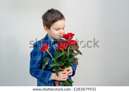 Adorable little boy in suit with a bouquet of red roses in hands on a light background, st. valentines day concept