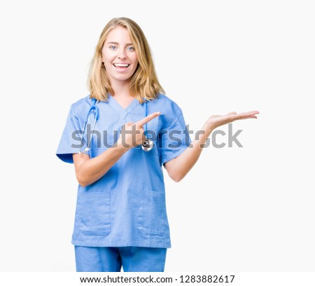 Beautiful young doctor woman wearing medical uniform over isolated background amazed and smiling to the camera while presenting with hand and pointing with finger.
