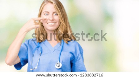 Beautiful young doctor woman wearing medical uniform over isolated background Pointing with hand finger to face and nose, smiling cheerful