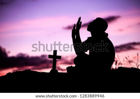 Boy sitting and praying with cross, christian silhouette concept.