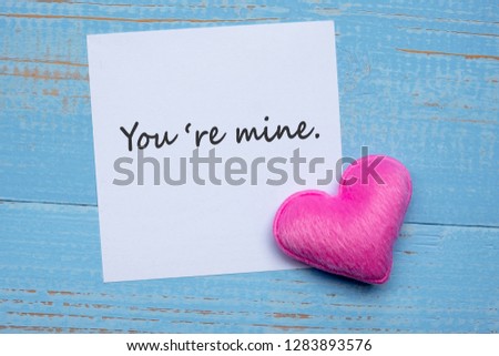 YOU'RE MINE word on paper note with pink heart shape decoration on blue wooden table background. Love, Wedding, Romantic and Happy Valentine’ s day holiday concept