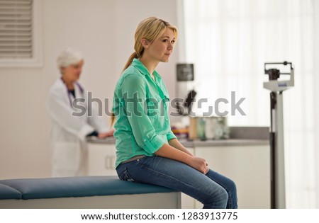 Contemplative young woman sitting inside a doctor's office with a female doctor.
