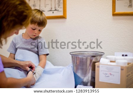 Young boy watching a nurse remove a bandage from his arm.
