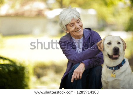 Smiling senior woman petting her dog in her garden.