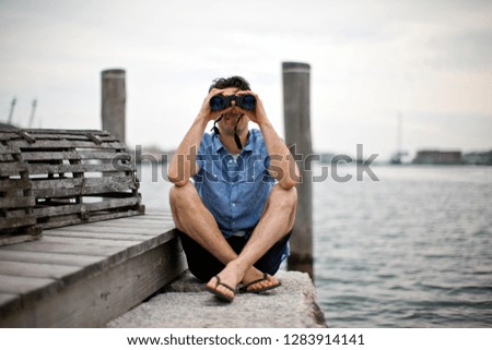 Man looking through binoculars at wharf.