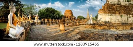 Row of seated Buddha statues and ancient temple ruins.