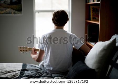 Boy sitting on bed playing guitar.