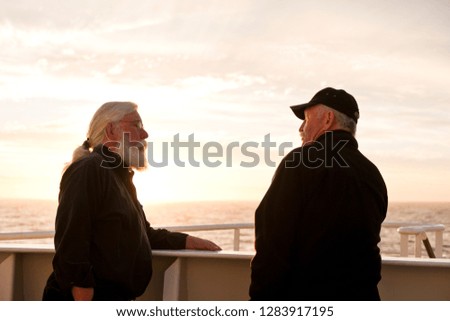 Two friends having a chat on the deck of a ship during sunset.