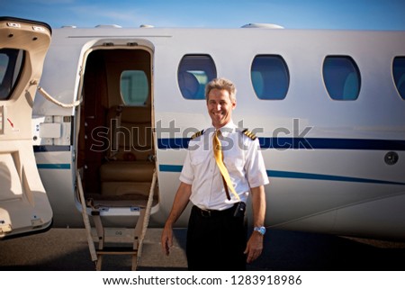 A pilot standing in front of a private jet and smiling