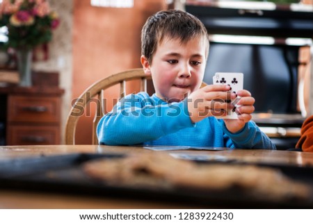 Young boy holding a handful of playing cards while seated at a table inside a cabin.