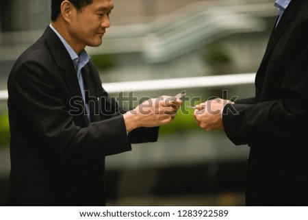 Two mid-adult businessmen exchanging business cards in the city.