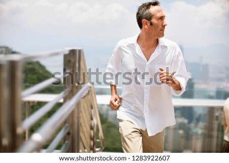 Mid-adult man wearing a white shirt walking up an outdoor staircase.