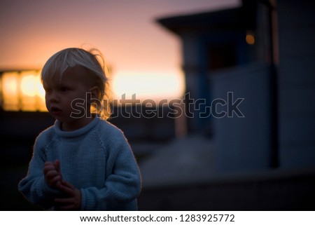 Young boy wearing a blue sweater outdoors at sunset.