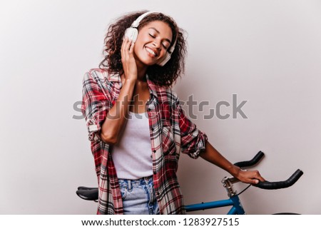 Pleasant black girl enjoying music with eyes closed. Appealing african lady listening favorite song during photoshoot with bicycle.
