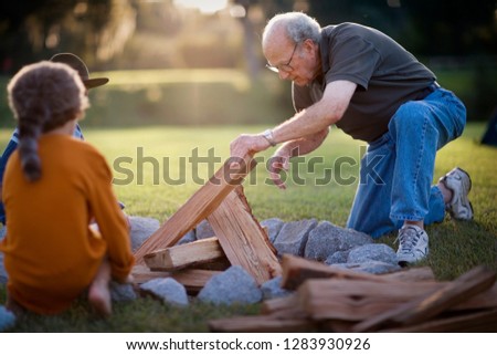 Senior man stacking chopped wood to make a fire with his two young grandsons.