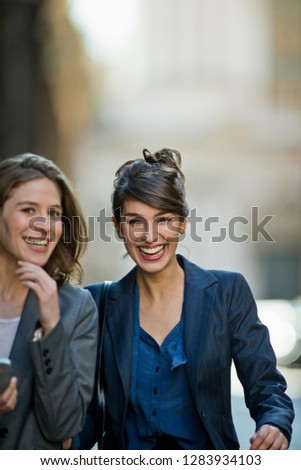 Two laughing young woman chat happily while walking home from the office.