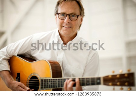 Portrait of a grinning mid adult man playing an acoustic guitar.