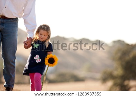 Young girl walking hand in hand with her father and carrying sunflower.
