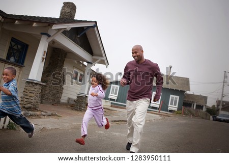 Smiling mid-adult father running down a suburban street with his two young children.