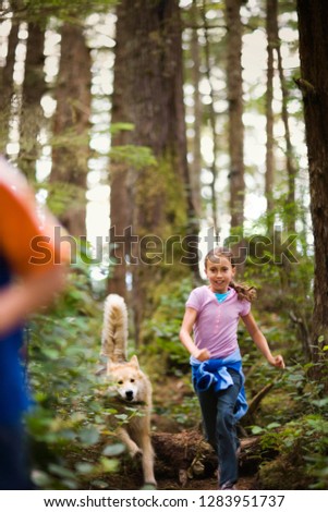 Young girl runs through a forest closely followed by her dog.
