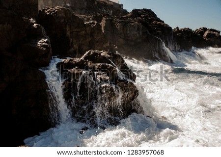 Stormy sea beating the rocks with a white waves with foam under the clear sky