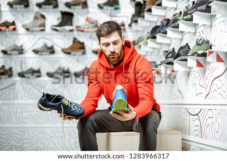 Man choosing trail shoes for hiking sitting in the fitting room of the modern sports shop Royalty-Free Stock Photo #1283966317