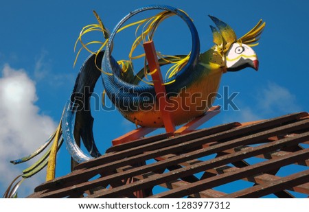 A bright multi-colored parrot made from a car tire by your own hands and painted with different colors, sitting on the roof against the blue sky.