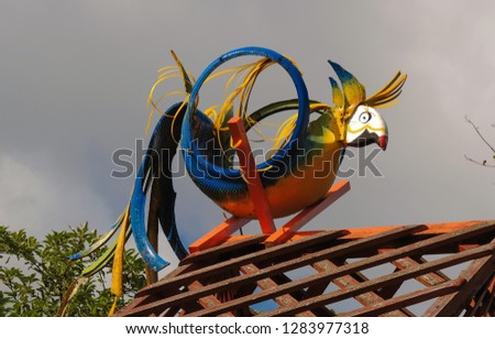 
A bright multi-colored parrot made from a car tire by your own hands and painted with different colors, sitting on the roof against the sky.