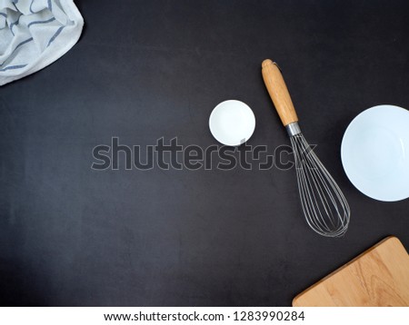 Ingredients concept of home cooking, Chopping Wood with Whisk and dish bowl on a dark granite table background. Copy space for text , Top view