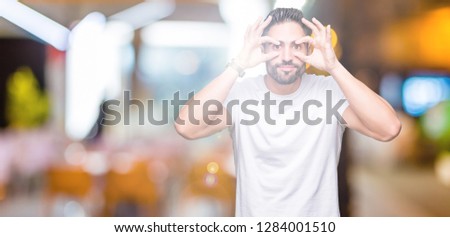 Handsome man wearing white t-shirt over night outdoors background Trying to open eyes with fingers, sleepy and tired for morning fatigue