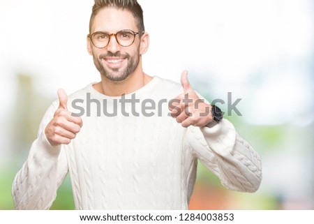 Young handsome man wearing glasses over isolated background success sign doing positive gesture with hand, thumbs up smiling and happy. Looking at the camera with cheerful expression, winner gesture.