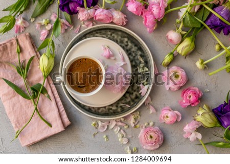 Upper view shot of a cup of coffee in the middle of floral frame of pink ranunculus and purple and yellow lisianthus