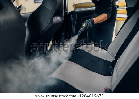 Carwash, worker cleans seats with steam cleaner Royalty-Free Stock Photo #1284015673