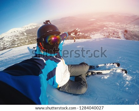 Winter extreme sport with selfie action camera. Man rides on slopes skis in protective helmet.