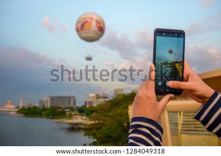 A woman is taking a picture of a hot air balloon flying into the sky using a mobile phone
