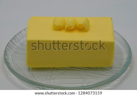 Delicious rolls of butter on a big block of butter. Butter is used for cooking and baking and it adds a tasty flavor to the food. Picture is ideal for advertising dairy products,