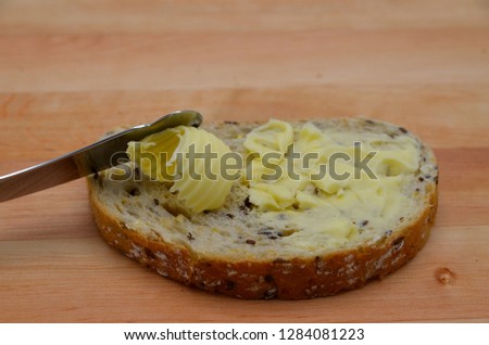 Butter being spread on a piece of bread. Butter is used for cooking and baking and it adds a tasty flavor to the food. Picture is ideal for advertising dairy products,