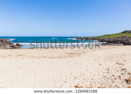 Beach cove with blue ocean wave waters to horizon with rocky coastline and green vegetation landscape
