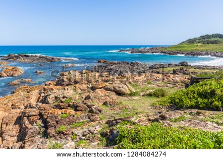 Beach cove with blue ocean wave waters to horizon with rocky coastline and green vegetation landscape