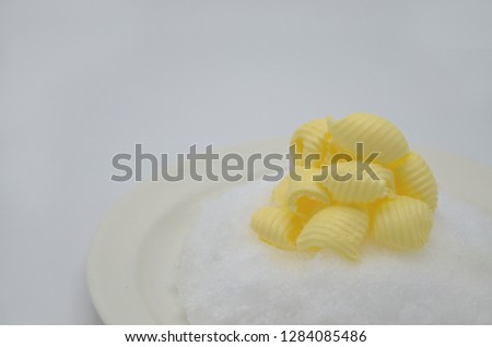 Delicious rolls of butter on a plate with snow. Butter is used for cooking and baking and it adds a tasty flavor to the food. Picture is ideal for advertising dairy products,